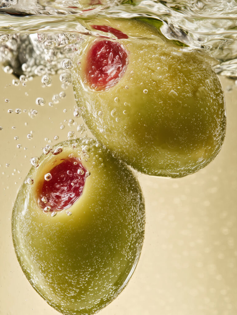 Close-up view of green olives underwater with visible bubbles, emphasizing surface texture and freshness.